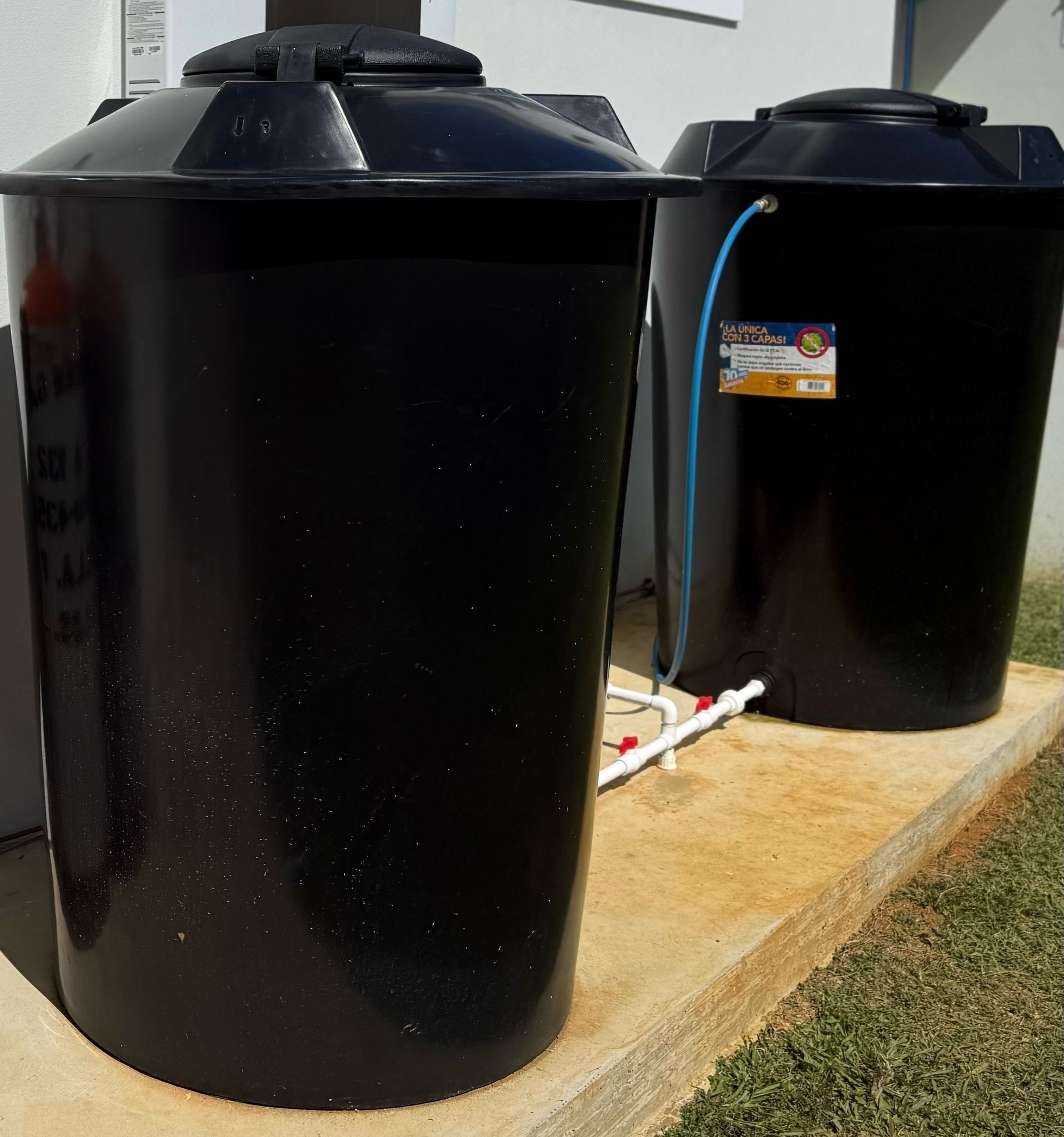 Zwei schwarze Wassertanks auf einer Holzplattform, im Hintergrund eine Rasenfläche.