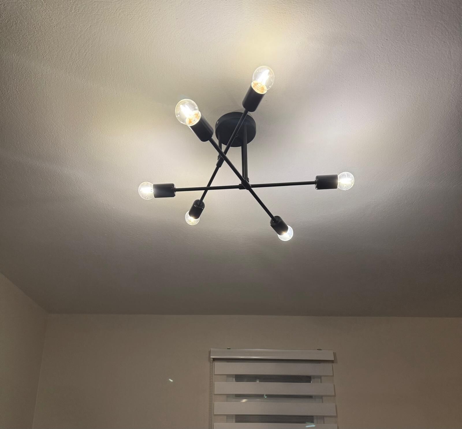 A ceiling with a black chandelier with multiple bulbs.