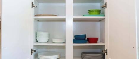 A cabinet with four shelves, each containing stacks of plates and bowls.