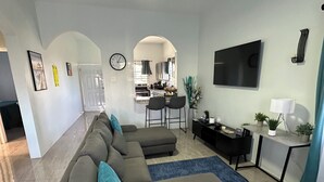A modern living room with a sectional sofa, a ceiling fan, a flat-screen TV, and a kitchen visible through an archway.