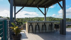 An outdoor bar area with a covered roof, a bar counter, and several stools.