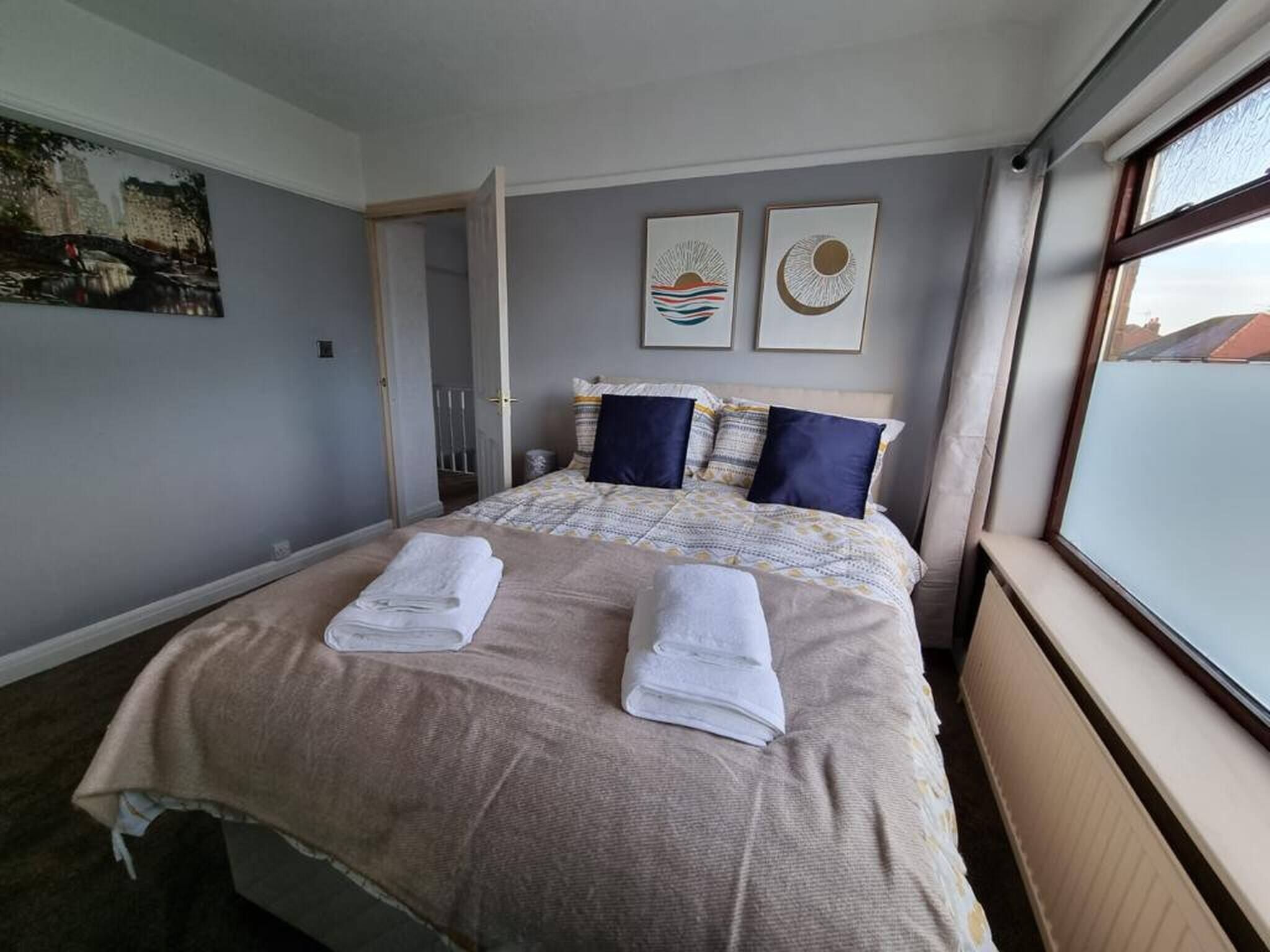 A hotel room with a large bed, two pillows, a blanket, and a window with a view.