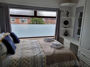 A bedroom with a bed, a bedside table, a mirror, and a view of a street outside. - 3 Bed Spacious House With Parking (Manchester)