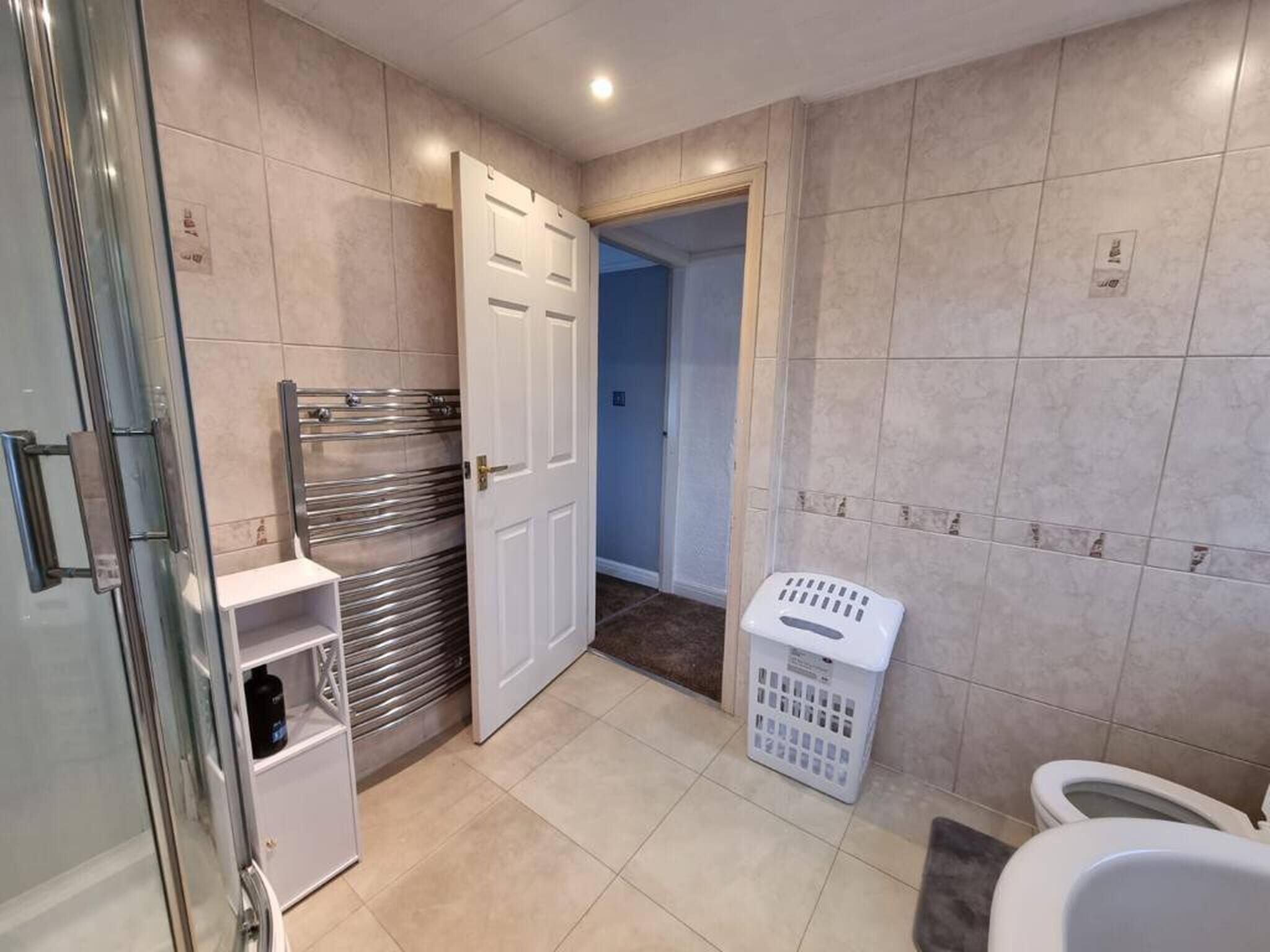 A bathroom with a glass shower enclosure, a white toilet, and a laundry basket.