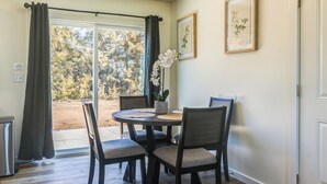 A dining area with a round table, four chairs, a potted orchid, and two framed botanical prints on the wall.