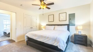 A bedroom with a bed, a ceiling fan, a nightstand with a lamp, and a door.