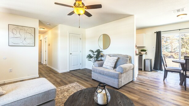 A modern living room with a ceiling fan, a gray sofa, a coffee table, and a dining area with a table and chairs.