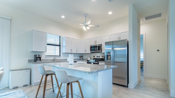 Una cocina moderna con armarios blancos, electrodomésticos de acero inoxidable y una isla central con taburetes de bar.
