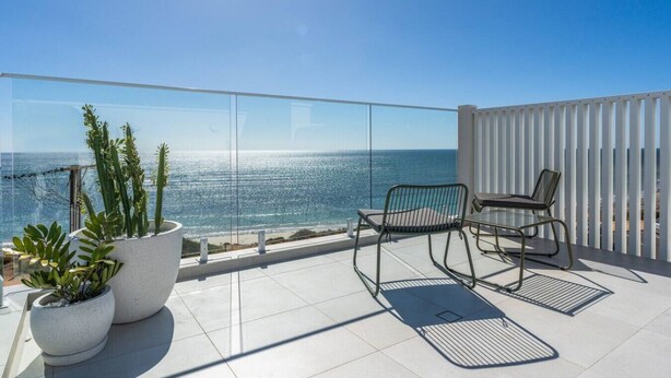 Een balkon met glazen hekwerk, twee stoelen en bloempotten.