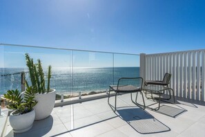 Un balcon doté d’une balustrade en verre, de deux chaises et de plantes en pot.