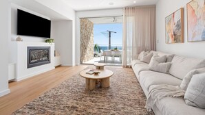 Een moderne woonkamer met een flatscreen televisie, een open haard, een bank en uitzicht op de oceaan door grote ramen.