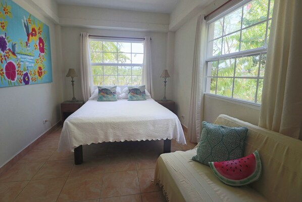 A bedroom with a bed, a sofa, a window, and a painting on the wall. - Waterfront tranquility: 3 Iguanas Villa- 1st floor Hibiscus Suite w rooftop pool (Placencia)