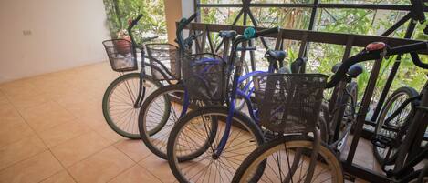 A row of bicycles parked indoors with a view of greenery outside.