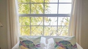A bed with two decorative pillows and a window with curtains. - Waterfront tranquility: 3 Iguanas Villa- 1st floor Hibiscus Suite w rooftop pool (Placencia)
