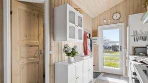 Une cuisine avec des murs en bois, un meuble blanc, une horloge et une vue sur l’extérieur.
