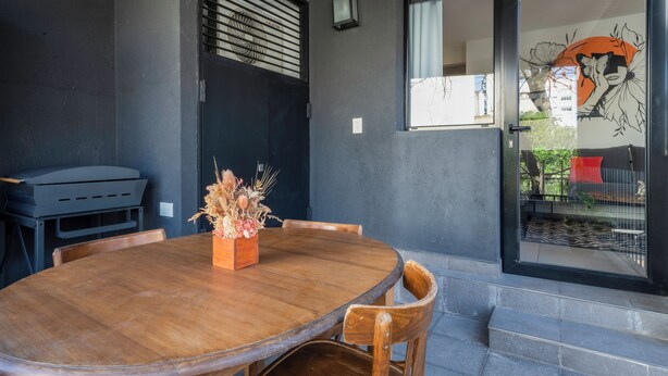 A dining area with a wooden table and chairs, a vase of dried flowers, and a grill outside. - FLIPHAUS Malabia 1900 (Buenos Aires)