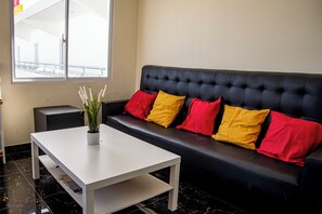 Ett modernt rum med en svart lädersoffa, ett vitt soffbord och en krukväxt.