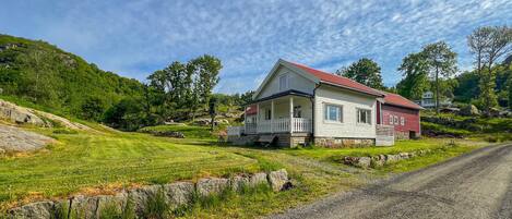 A two-story house with a porch, surrounded by a grassy landscape and a dirt road.