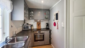 A compact kitchen with a double sink, a microwave, a coffee maker, and a wooden cutting board with a logo. - 3 bedroom cozy home in Farsund (Farsund)