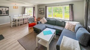 A modern living room with a grey sectional sofa, a white coffee table, and a dining area with a white table and chairs. - 3 bedroom cozy home in Farsund (Farsund)