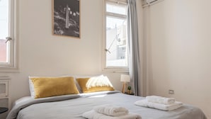 A neatly made bed with white linens and two folded towels, a bedside table with a lamp, and a window with curtains. - MOT Maipu 800 (Buenos Aires)