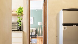 A narrow hallway with a refrigerator on the right, a bed with a lamp in the background, and a plant on a shelf. - MOT Maipu 800 (Buenos Aires)