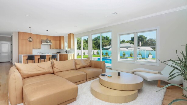 Ein modernes Wohnzimmer mit einer Eckcouch, einem runden Couchtisch und Blick auf einen Swimmingpool durch große Fenster.
