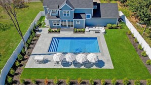 Ein zweigeschossiges Haus mit Swimmingpool, einer Terrasse und Gartenmöbeln sowie einem gepflegten Rasen.