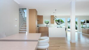 Eine moderne Küche mit Holzausstattung, einer zentralen Kochinsel und einem Essbereich mit langem Tisch und weißen Stühlen.