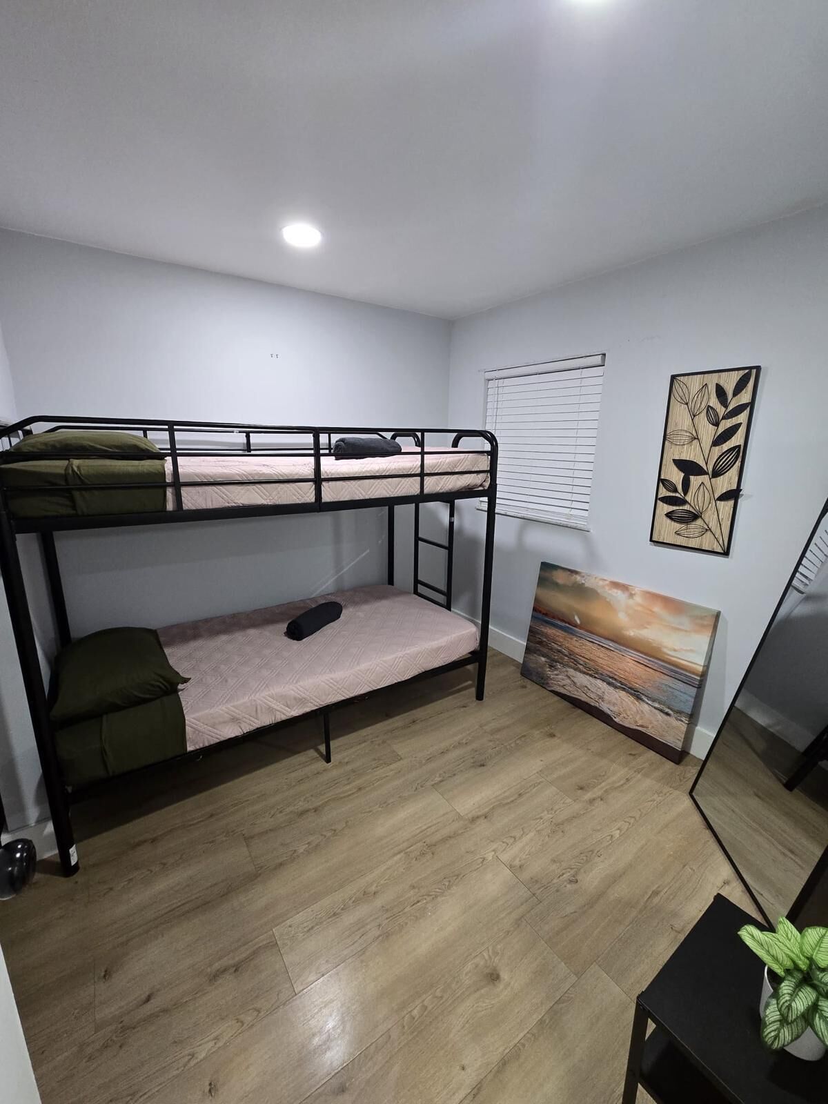 A bunk bed room with a wooden floor, a small table with a plant, and a painting on the wall.