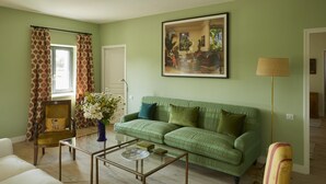 A living room with a green sofa, a glass coffee table, and a chair with a patterned cushion. - Gîtes de France® - La Maison d'Irène (DOUDEVILLE)