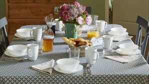 A dining table set with white dishes, a vase of flowers, and a lamp. - Gîtes de France® - La Maison d'Irène (DOUDEVILLE)