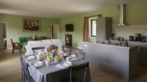 A modern kitchen with a central island, a dining area with a table set for two, and a living room with a sofa and a painting. - Gîtes de France® - La Maison d'Irène (DOUDEVILLE)