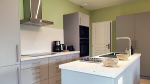 A modern kitchen with grey cabinets, a stainless steel range hood, a built-in oven, and a sink with a faucet. - Gîtes de France® - La Maison d'Irène (DOUDEVILLE)