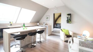 Una cocina moderna con una isla central, taburetes de bar y una zona de comedor con un sofá blanco y una mesa.