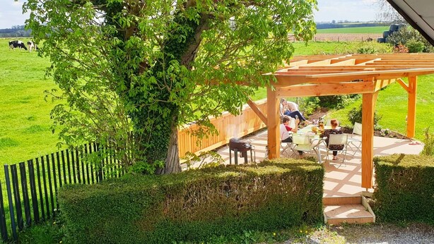 Un patio techado al aire libre con una pérgola de madera, una parrilla y una mesa de comedor con sillas.