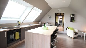 Cocina moderna con una isla grande, tragaluces y un comedor con una silla y mesa blancos.