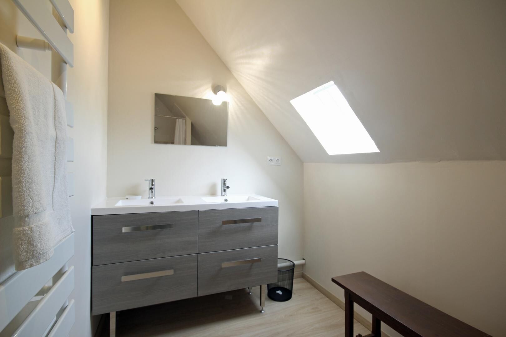 Une petite salle de bain moderne avec un puits de lumière, un meuble-lavabo doté de deux vasques et un banc.