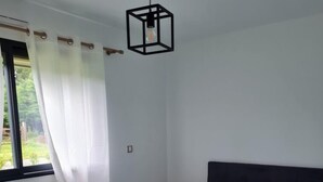 Makuuhuone, jossa on sänky, ikkuna verhoilla, patteri ja riippuvalaisin.