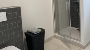 Kylpyhuone, jossa on wc, roskakori ja lasiseinällä erotettu suihkutila.