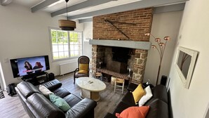 A living room with a fireplace, leather sofas, a TV, and a dining area. - Gîtes de France® - Le Gîte du Moulin (SAINT PIERRE LE VIEUX)