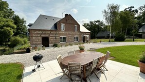 A brick house with a large patio, a barbecue grill, and a round wooden table with chairs. - Gîtes de France® - Le Gîte du Moulin (SAINT PIERRE LE VIEUX)