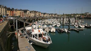 A marina with boats docked, a wooden pier, and buildings in the background. - Gîtes de France® - Le Gîte du Moulin (SAINT PIERRE LE VIEUX)