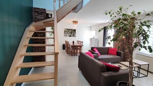 Una sala de estar moderna con una escalera, un comedor y un gran árbol en maceta.