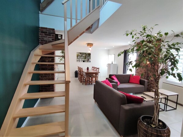 A modern living room with a staircase, a dining area, and a large potted tree.
