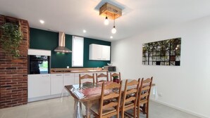 Cocina moderna con armarios blancos, pared decorativa de ladrillo y comedor con sillas y mesa de madera.