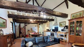 A cozy living room with a dark leather sofa, wooden coffee table, and a dining area with a wooden table and chairs. A kitchen with modern appliances is visible in the background.