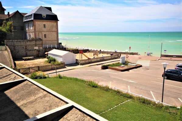 A coastal view with a beach, a parking area, and a building with a sloped roof.