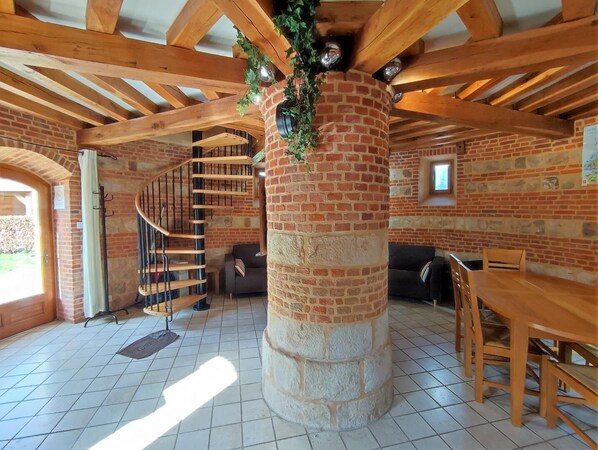 A spacious living area with a brick column, a wooden staircase, a dining table, and a sofa.