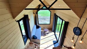 Ein Loft-Zimmer mit Holzvertäfelung, einer Couch, einem kleinen Tisch und einer Essecke mit Uhr und Pendelleuchten.